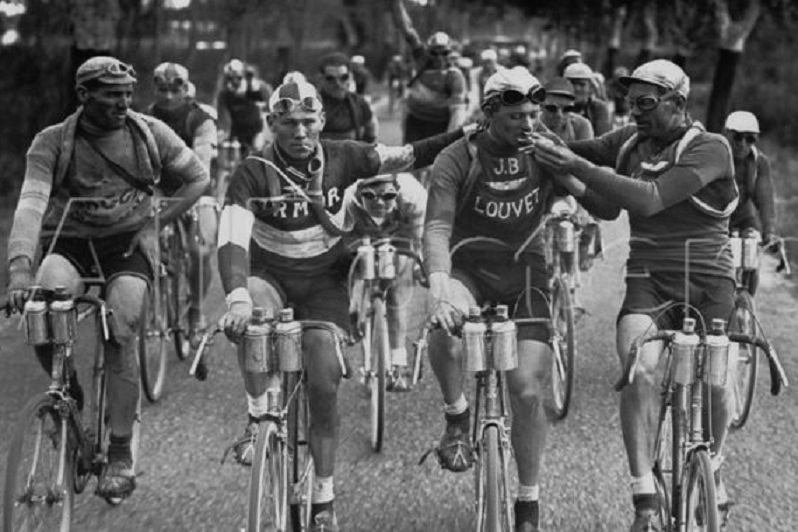 Four cyclists riding together at the front of the pelotom at the Tour de France in 1927. One of them lighting a cigarette. 